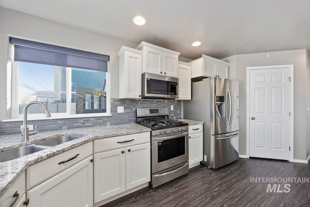 kitchen featuring sink, dark wood-type flooring, light stone counters, white cabinets, and appliances with stainless steel finishes