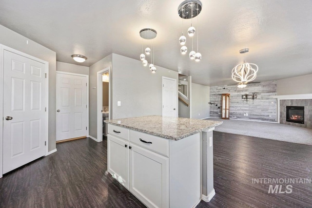 kitchen with pendant lighting, light stone counters, white cabinetry, and a tile fireplace