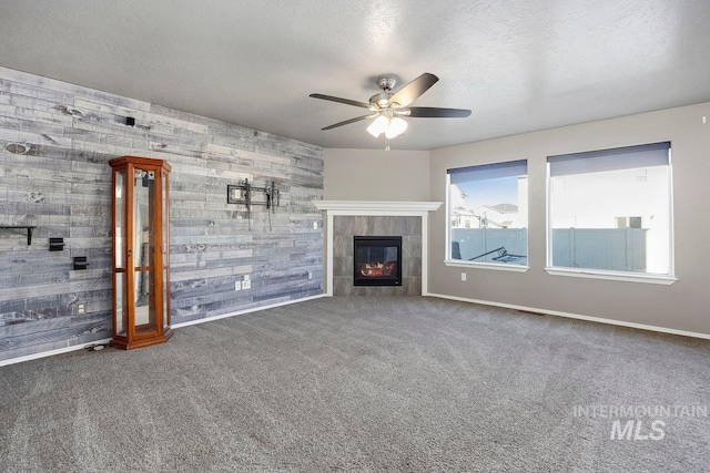 unfurnished living room with wood walls, dark colored carpet, ceiling fan, a textured ceiling, and a tiled fireplace