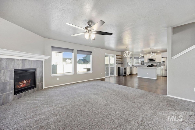 unfurnished living room featuring a tiled fireplace, ceiling fan, dark carpet, and a textured ceiling