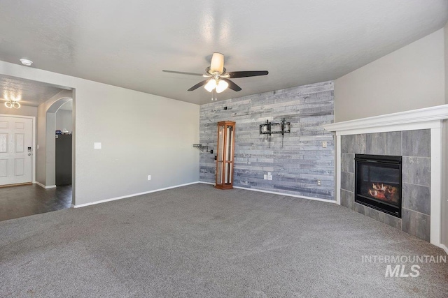 unfurnished living room with ceiling fan, wood walls, a fireplace, and dark carpet