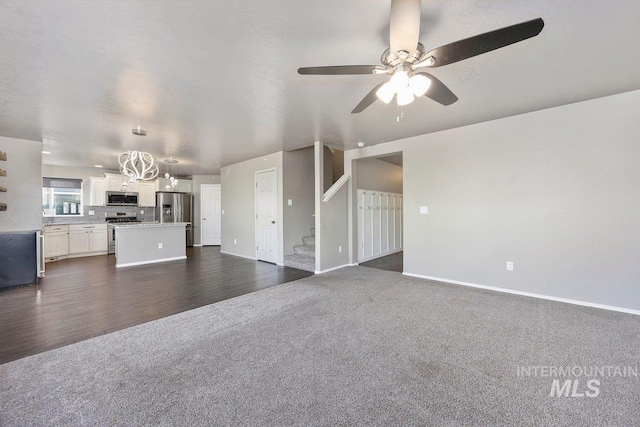 unfurnished living room with dark carpet and ceiling fan with notable chandelier