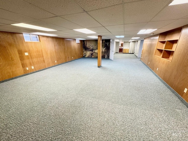 finished basement with wooden walls, carpet flooring, and a drop ceiling