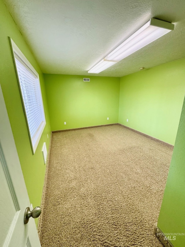 empty room with visible vents, baseboards, a textured ceiling, and carpet flooring