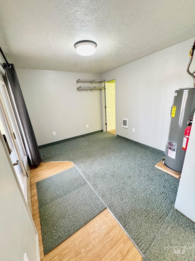 empty room with visible vents, gas water heater, carpet flooring, wood finished floors, and a textured ceiling