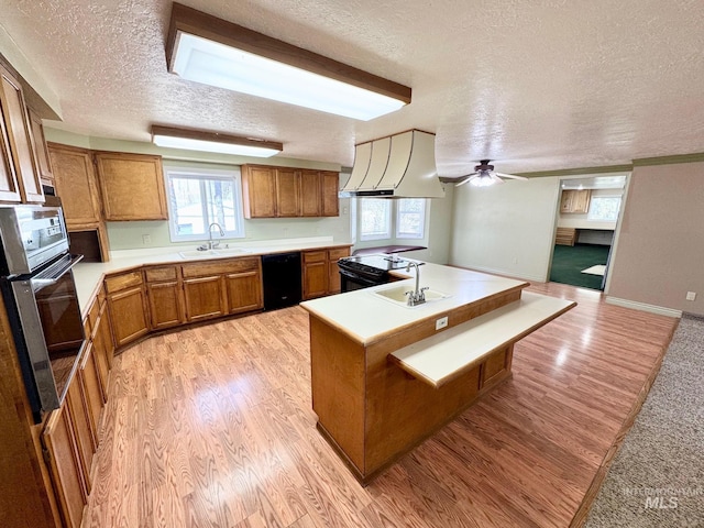 kitchen with light wood finished floors, ventilation hood, brown cabinetry, black appliances, and a sink