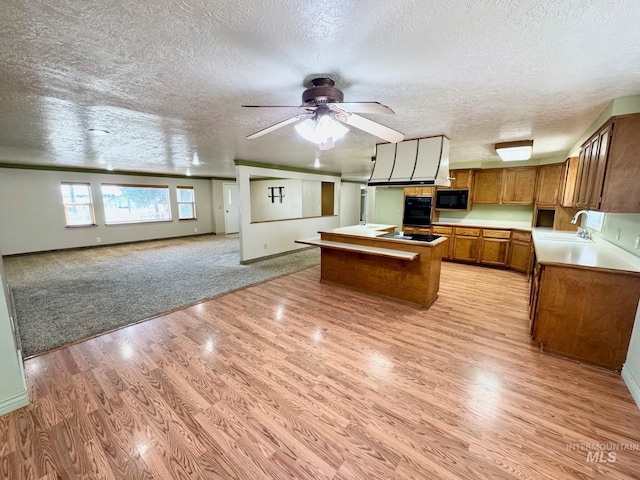 kitchen with black appliances, a sink, open floor plan, light wood-style floors, and brown cabinetry