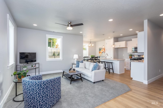 living room with ceiling fan with notable chandelier, a textured ceiling, and light wood-type flooring