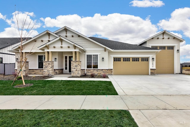 view of front of house featuring a front lawn, roof with shingles, driveway, stone siding, and an attached garage