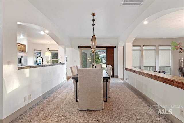 dining area featuring arched walkways, baseboards, visible vents, and light carpet