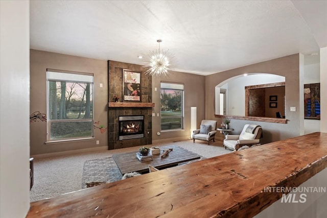 carpeted living room with a tiled fireplace, an inviting chandelier, and baseboards