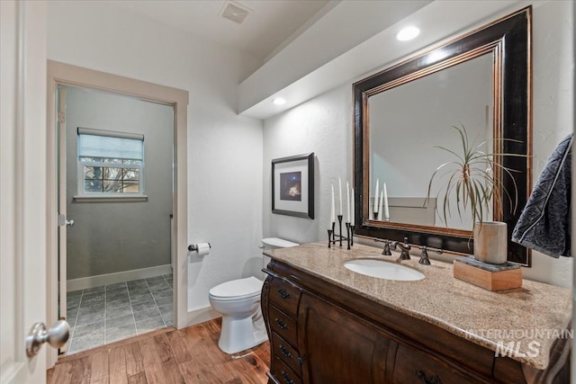 bathroom with vanity, wood finished floors, visible vents, baseboards, and toilet