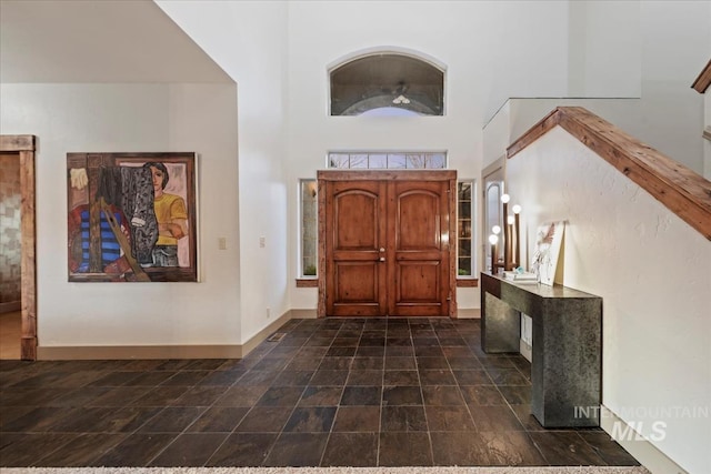 entryway featuring stone finish flooring, baseboards, and a towering ceiling