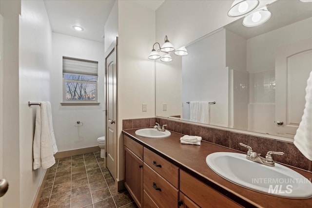 full bathroom featuring double vanity, toilet, baseboards, and a sink