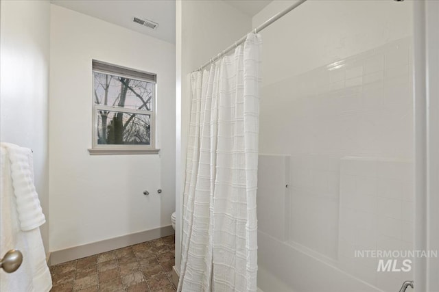 full bathroom featuring visible vents, baseboards, toilet, shower / bath combo, and stone finish floor