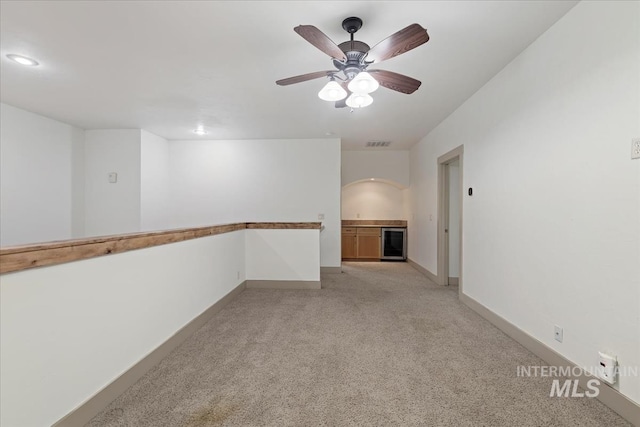 unfurnished room featuring visible vents, light carpet, wine cooler, baseboards, and ceiling fan