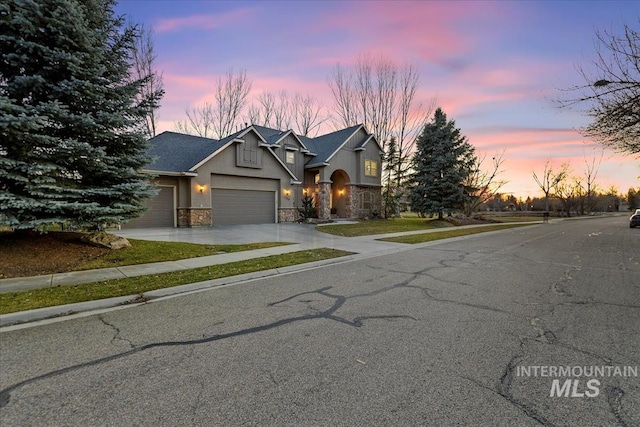 view of front of home featuring driveway, a shingled roof, stucco siding, a garage, and stone siding