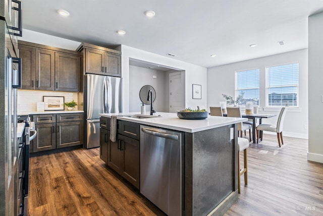 kitchen with a sink, dark wood finished floors, stainless steel appliances, light countertops, and decorative backsplash