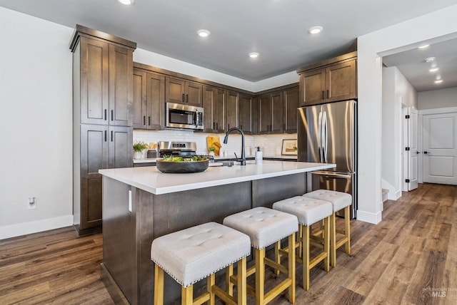 kitchen featuring stainless steel appliances, tasteful backsplash, dark wood-style flooring, and light countertops