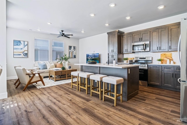 kitchen featuring a kitchen bar, a center island with sink, dark wood-style floors, stainless steel appliances, and light countertops