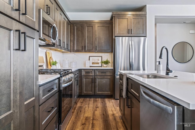 kitchen featuring backsplash, light countertops, dark wood-style flooring, appliances with stainless steel finishes, and a kitchen island with sink