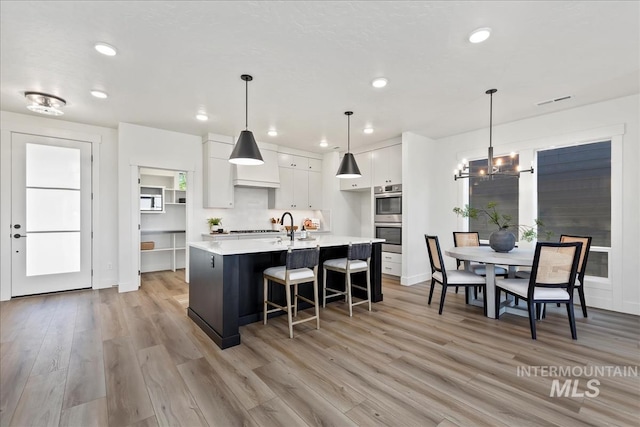 kitchen with double oven, white cabinetry, light hardwood / wood-style flooring, and decorative light fixtures