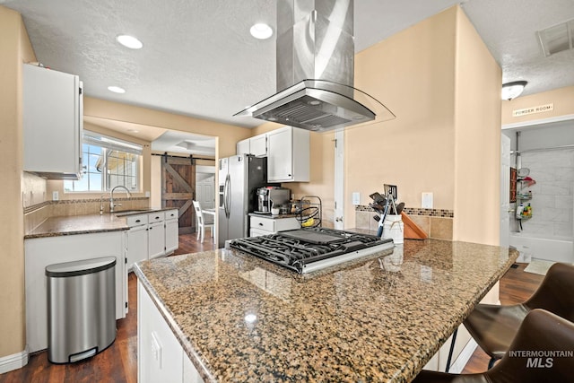 kitchen with white cabinetry, dark stone countertops, sink, island range hood, and a barn door