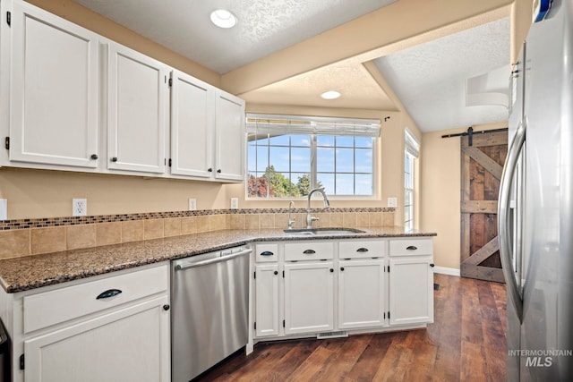 kitchen featuring appliances with stainless steel finishes, sink, white cabinets, dark stone counters, and a barn door