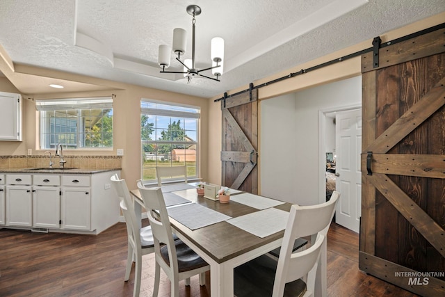 dining space featuring sink, dark hardwood / wood-style flooring, a barn door, and a textured ceiling