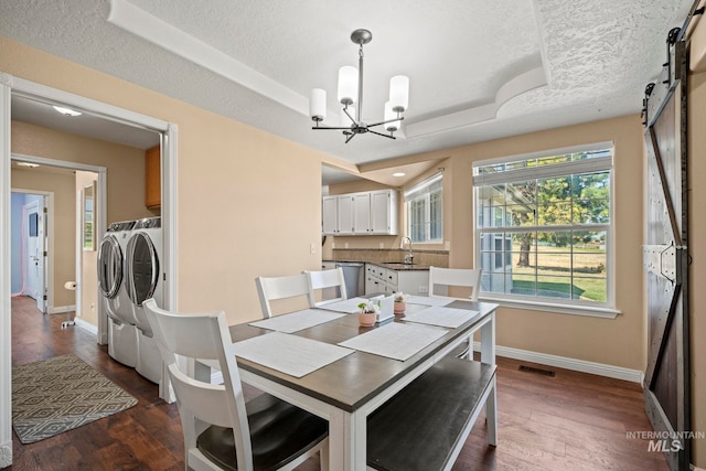 dining area featuring sink, a tray ceiling, a barn door, separate washer and dryer, and a textured ceiling