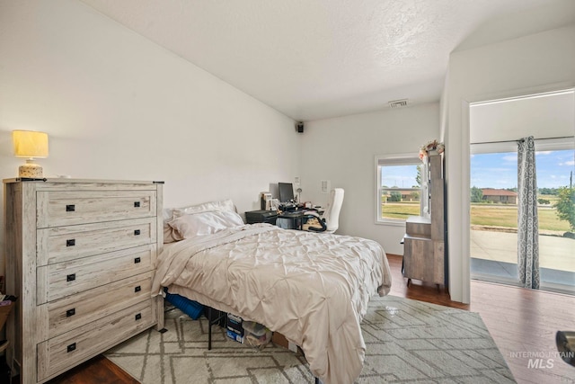 bedroom with access to outside, a textured ceiling, and wood-type flooring