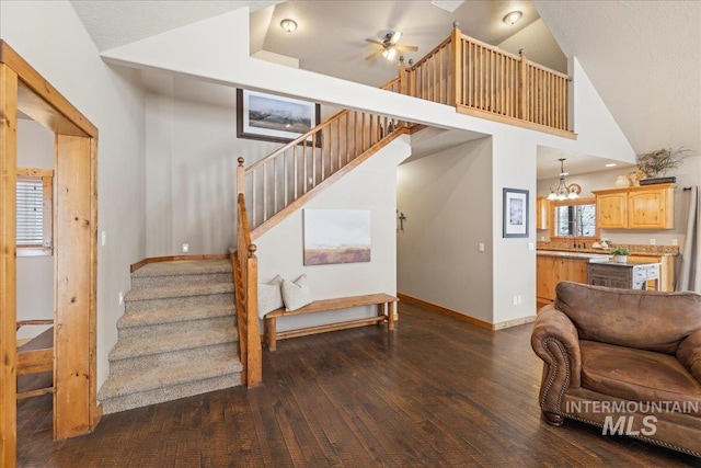 staircase with high vaulted ceiling, ceiling fan with notable chandelier, and hardwood / wood-style flooring