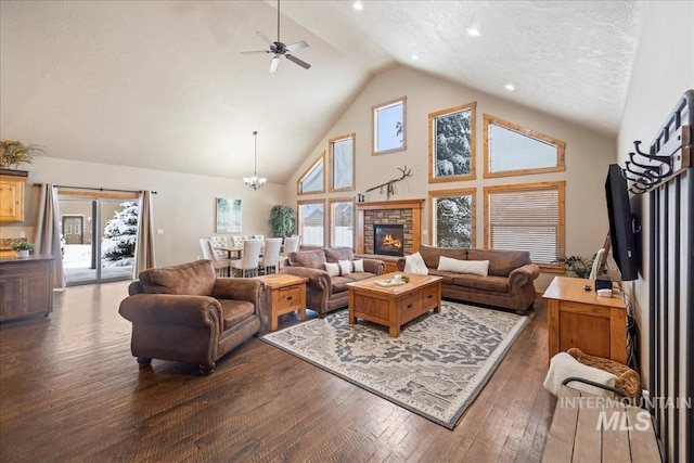 living room with dark hardwood / wood-style flooring, ceiling fan with notable chandelier, a textured ceiling, high vaulted ceiling, and a fireplace