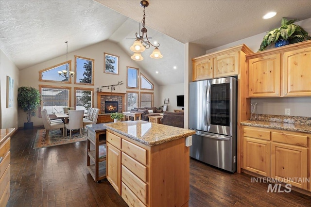 kitchen featuring pendant lighting, lofted ceiling, a notable chandelier, light stone counters, and stainless steel refrigerator