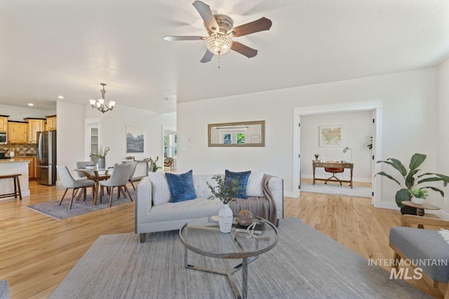 living room featuring a chandelier, light wood-style flooring, a ceiling fan, and baseboards