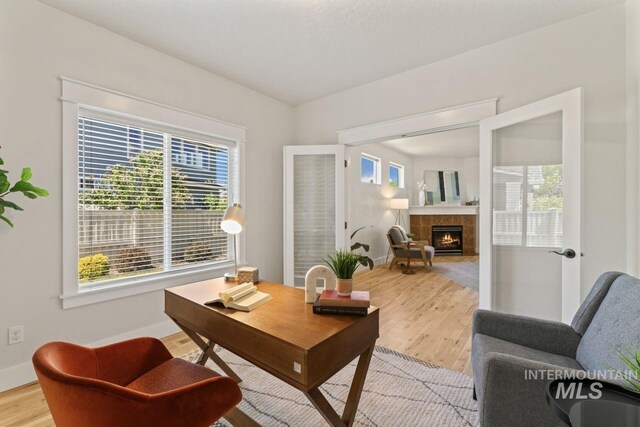 office area with light wood finished floors, plenty of natural light, baseboards, and a tile fireplace