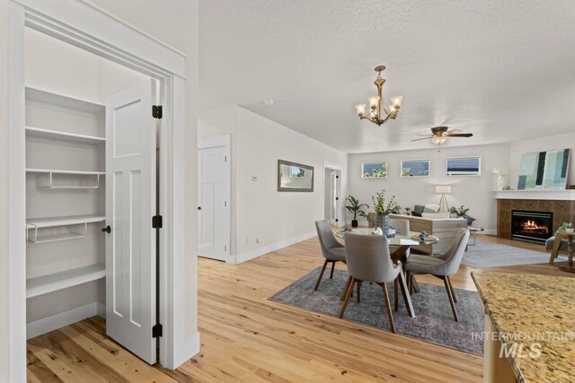 dining space featuring a chandelier, a fireplace, light wood-style flooring, ceiling fan, and a textured ceiling