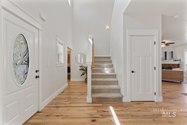 foyer entrance with light wood-type flooring, ceiling fan, stairway, and baseboards