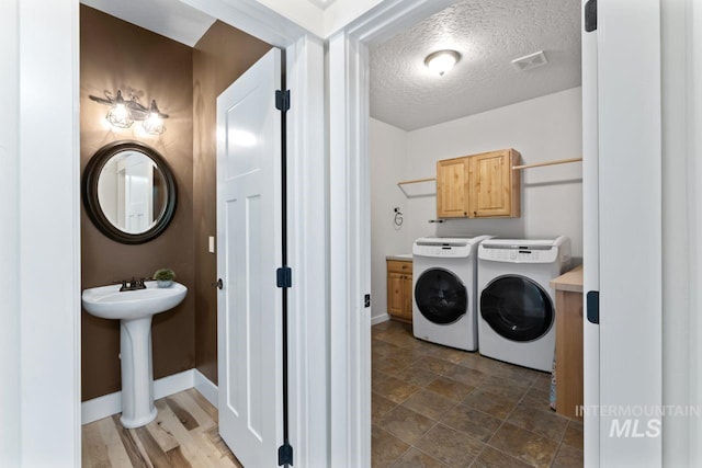 washroom with washer and dryer, baseboards, cabinet space, and a textured ceiling