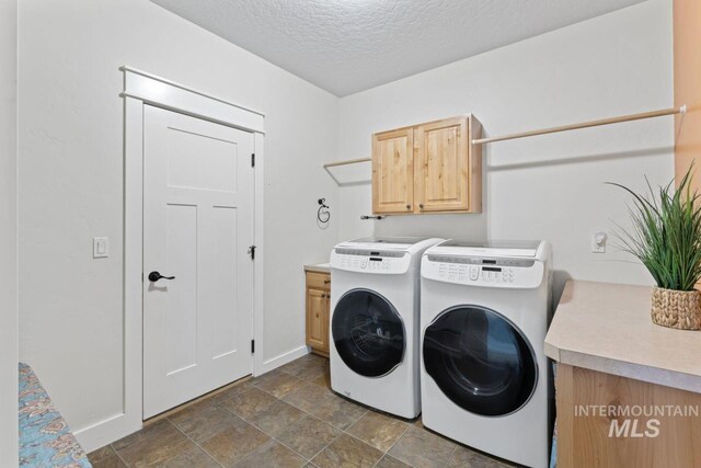 clothes washing area with independent washer and dryer, cabinet space, a textured ceiling, baseboards, and stone finish floors