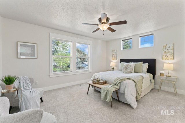 bedroom with baseboards, a textured ceiling, light carpet, and ceiling fan