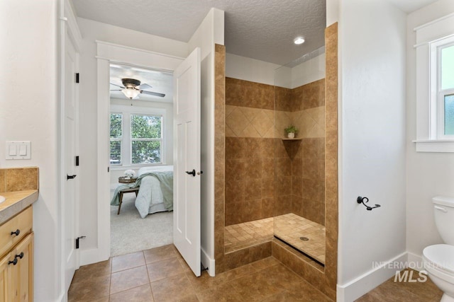 full bathroom with toilet, a tile shower, vanity, tile patterned floors, and baseboards