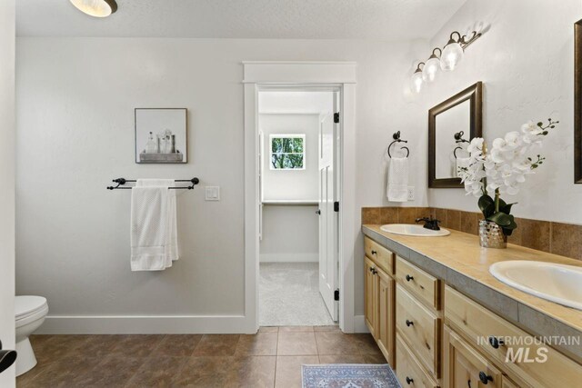 full bathroom featuring baseboards, double vanity, toilet, and tile patterned flooring