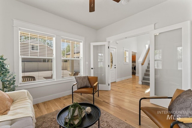 living area featuring stairs, light wood-style floors, baseboards, and a ceiling fan