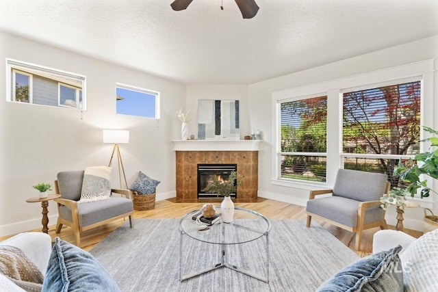 living area featuring a ceiling fan, baseboards, a tiled fireplace, and wood finished floors