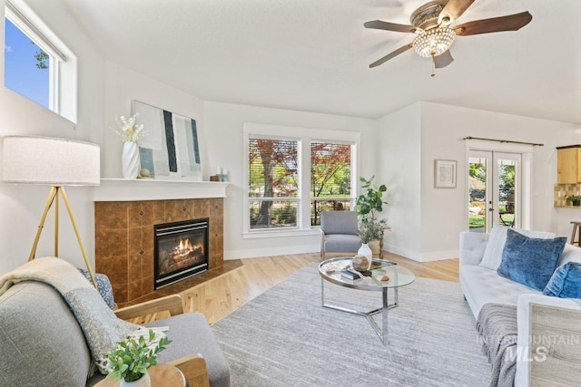 living room featuring a tiled fireplace, wood finished floors, ceiling fan, baseboards, and french doors