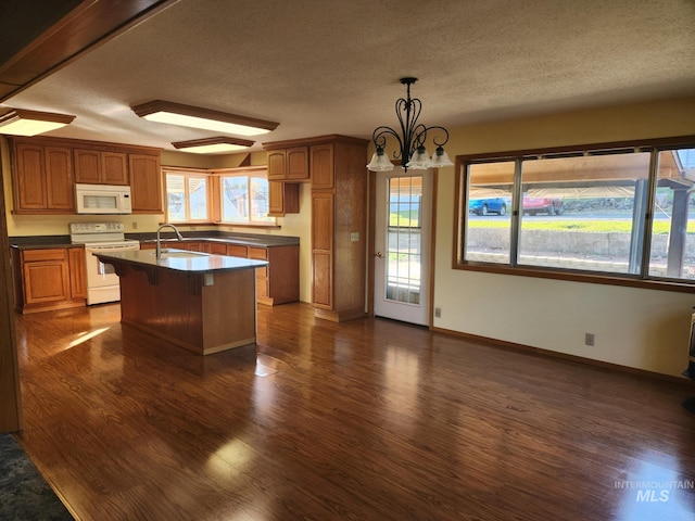 kitchen featuring a healthy amount of sunlight, white appliances, a kitchen island with sink, and dark hardwood / wood-style floors