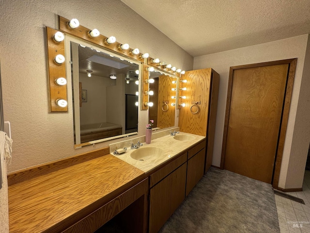 full bathroom with double vanity, a textured ceiling, a sink, and a textured wall