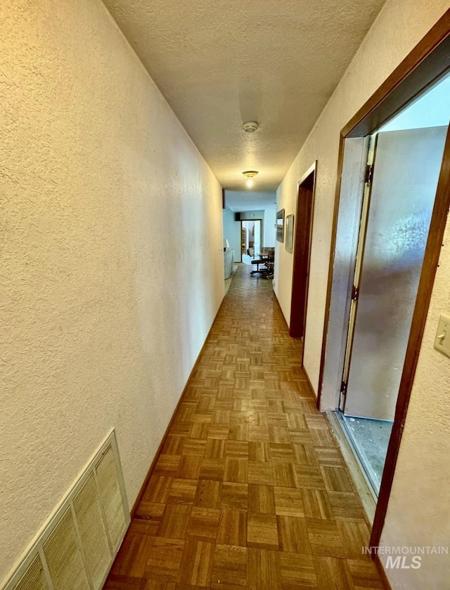 hallway featuring visible vents, a textured wall, and a textured ceiling