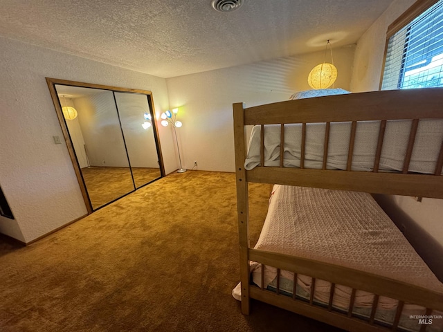 bedroom featuring a textured ceiling, visible vents, carpet flooring, and a textured wall